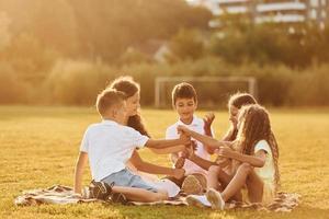 miteinander kommunizieren. Eine Gruppe glücklicher Kinder ist tagsüber draußen auf dem Sportplatz foto