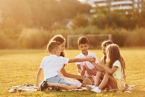 schönes Sonnenlicht. eine gruppe glücklicher kinder ist tagsüber draußen auf dem sportplatz foto