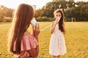 kinder, die spaß mit blechdosentelefon haben. Stehen im Freien auf dem Sportplatz foto