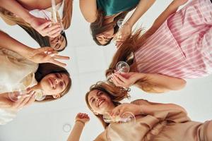 Getränke halten und nach unten schauen. Gruppe glücklicher Frauen, die auf einem Junggesellinnenabschied sind foto