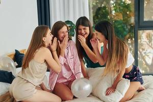 auf dem Bett sitzen. Gruppe glücklicher Frauen, die auf einem Junggesellinnenabschied sind foto