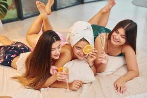 sich mit Orangenscheiben aufs Bett legen. Gruppe glücklicher Frauen, die auf einem Junggesellinnenabschied sind foto