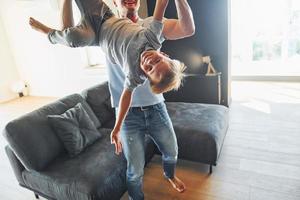 Mann, der Jungen hält und Spaß hat. Vater und Sohn sind zusammen zu Hause foto