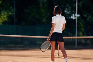 gegen Bäume im Hintergrund. Tennisspielerin ist tagsüber auf dem Platz foto