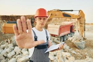 Stoppschild von Hand zeigen. Arbeiter in Berufsuniform ist tagsüber in der Leihgrube foto