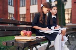 Bücher und Äpfel. Zwei Schulmädchen sind draußen zusammen in der Nähe des Schulgebäudes foto