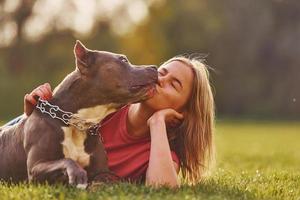 sich auf den Boden legen. Frau in Freizeitkleidung ist mit Pitbull im Freien foto