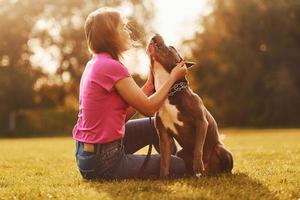 den Hund umarmen. Frau in Freizeitkleidung ist mit Pitbull im Freien foto