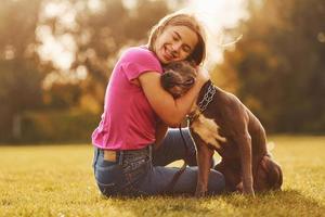 den Hund umarmen. Frau in Freizeitkleidung ist mit Pitbull im Freien foto