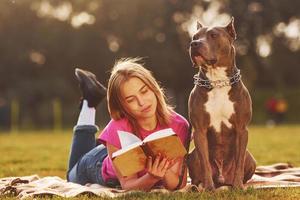 das Buch lesen. Frau in Freizeitkleidung ist mit Pitbull im Freien foto