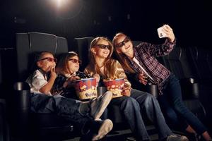 Selfies machen. gruppe von kindern, die im kino sitzen und zusammen filme ansehen foto