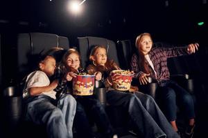 auf den schwarzen Sitzen sitzen. gruppe von kindern, die im kino sitzen und zusammen filme ansehen foto