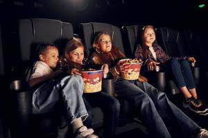 auf den schwarzen Sitzen sitzen. gruppe von kindern, die im kino sitzen und zusammen filme ansehen foto