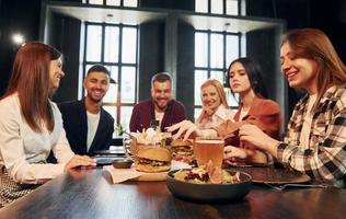 in Freizeitkleidung. gruppe junger freunde, die zusammen in der bar mit bier sitzen foto