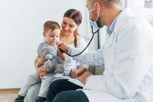 Der kleine Junge wird untersucht. Zwei Ärzte in weißen Kitteln arbeiten in der Klinik zusammen foto