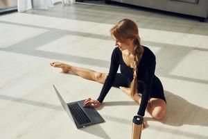 silberfarbener Laptop. Frau in sportlicher Kleidung, die drinnen Yoga macht foto