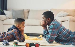 zusammen spielen. Afroamerikanischer Vater mit seinem kleinen Sohn zu Hause foto