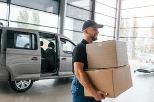 Arbeitstag. lieferbote in uniform ist drinnen mit auto und mit bestellung foto