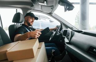 mit Fahrzeug. lieferbote in uniform ist drinnen mit auto und mit bestellung foto