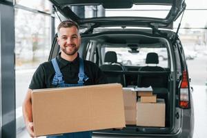 Haltekiste. lieferbote in uniform ist drinnen mit auto und mit bestellung foto