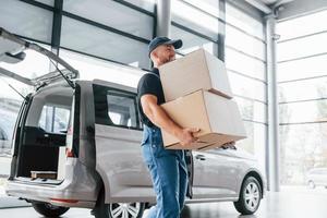 Arbeitstag. lieferbote in uniform ist drinnen mit auto und mit bestellung foto