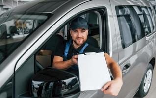 im Fahrzeug sitzen und Dokument halten. lieferbote in uniform ist drinnen mit auto und mit bestellung foto