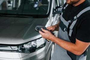 Werkzeuge in den Händen. Mann in Uniform arbeitet tagsüber im Autosalon foto