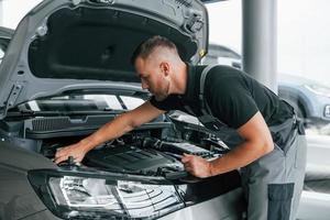 unter der Haube. Mann in Uniform arbeitet tagsüber im Autosalon foto