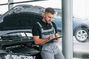 mit Notizblock. Mann in Uniform arbeitet tagsüber im Autosalon foto