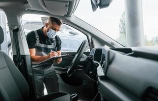 Qualitätskontrolle. Mann in Uniform arbeitet tagsüber im Autosalon foto