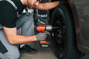 Wechsel der Reifen. Mann in Uniform arbeitet tagsüber im Autosalon foto