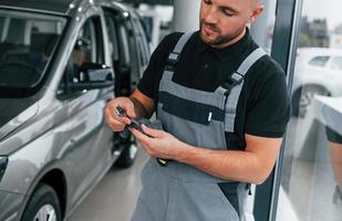 Werkzeuge in den Händen. Mann in Uniform arbeitet tagsüber im Autosalon foto