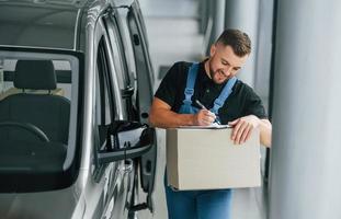 in blauer Kleidung. lieferbote in uniform ist drinnen mit auto und mit bestellung foto