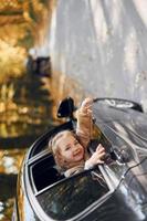 kleines Mädchen, das im schwarzen Auto sitzt und durch das Fenster schaut foto