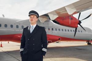 pilot in formeller schwarzer uniform steht draußen in der nähe des flugzeugs foto