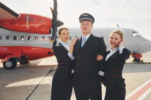 Pilot und zwei Stewardessen. Besatzung von Flughafen- und Flugzeugarbeitern in formeller Kleidung, die zusammen im Freien stehen foto