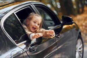 kleines Mädchen, das im schwarzen Auto sitzt und durch das Fenster schaut foto