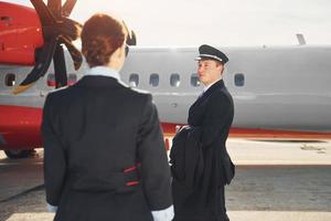 Pilot und Stewardess. Besatzung von Flughafen- und Flugzeugarbeitern in formeller Kleidung, die zusammen im Freien stehen foto