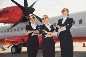 drei Stewardessen. Besatzung von Flughafen- und Flugzeugarbeitern in formeller Kleidung, die zusammen im Freien stehen foto