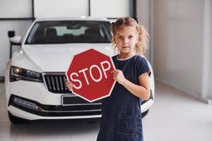 Porträt eines süßen kleinen Mädchens, das im Autosalon ein Straßenschild in den Händen hält foto