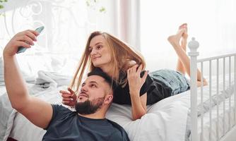 junges Ehepaar macht tagsüber ein Selfie mit dem Telefon im Schlafzimmer foto