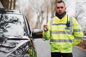 männlicher polizist in grüner uniform, der mit handschellen in der nähe des autos steht foto