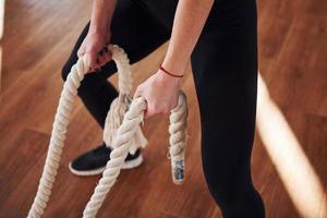 Nahaufnahme einer sportlichen jungen Frau in schwarzer sportlicher Kleidung, die mit Knoten in den Händen im Fitnessstudio steht foto