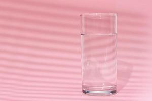 Glas Wasser auf einem rosa Hintergrund foto