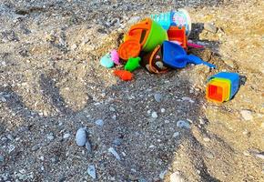 Sand am Strand mit Steinen und Erde. Meeresküste, auf dem Boden stehen ein Eimer mit Kinderspielzeug, Formen für Sand. Unterhaltung für Kleinkinder, Kinderspiel foto