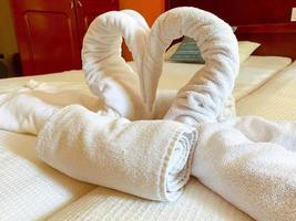 Ruhe am Meer in einem teuren Hotel. Beim Reinigen des Zimmers legte der Arbeiter Schwäne aus weißen Handtüchern in Form eines Herzens aus foto