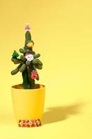 kaktus verziert mit kleinen weihnachtssymbolen als alternativer weihnachtsbaum auf gelb. vertikale Ausrichtung. foto
