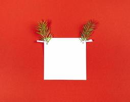 kreatives weihnachtliches hirschgesicht aus weißem quadratischem blech und zwei tannenzweigen als rentiergeweih auf rot foto