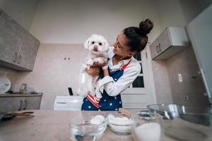 lächelnde frau in der küche, die niedlichen weißen malteserhund hält foto