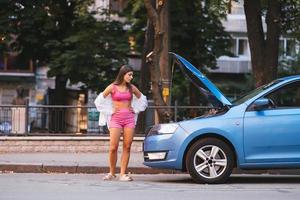 Frau mit kaputtem Auto auf der Straße. Hilfe suchen. foto